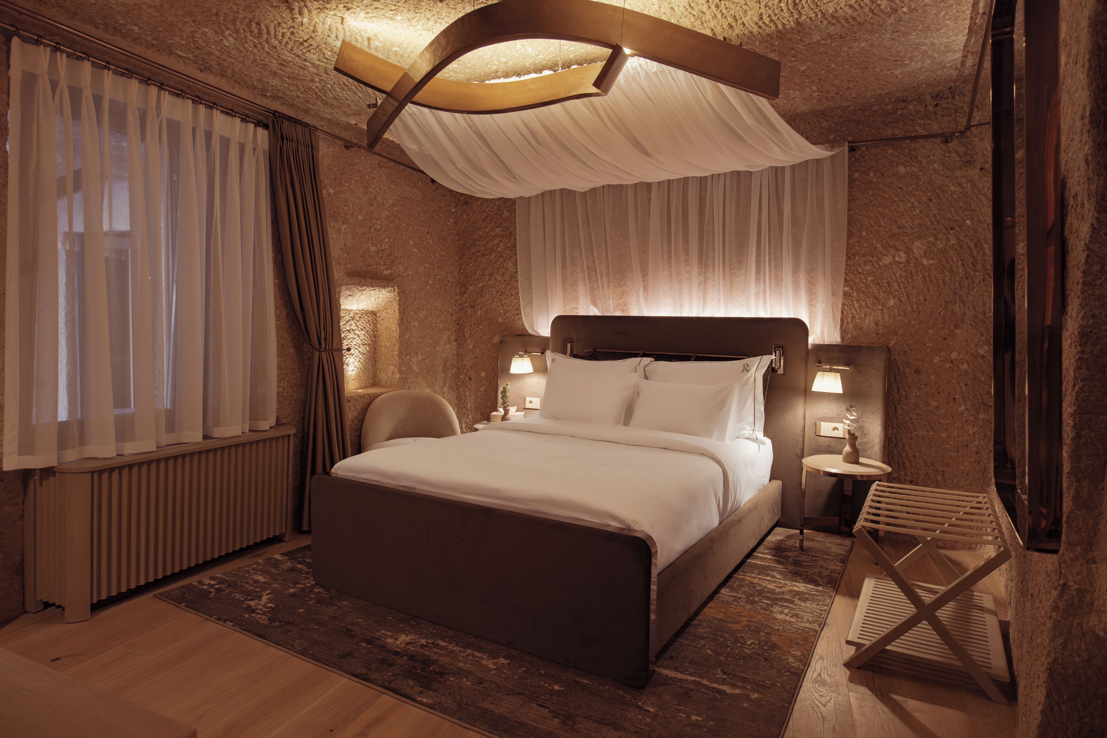 Quarto com cama grande, luminárias laterais, uma cadeira de madeira e radiador.