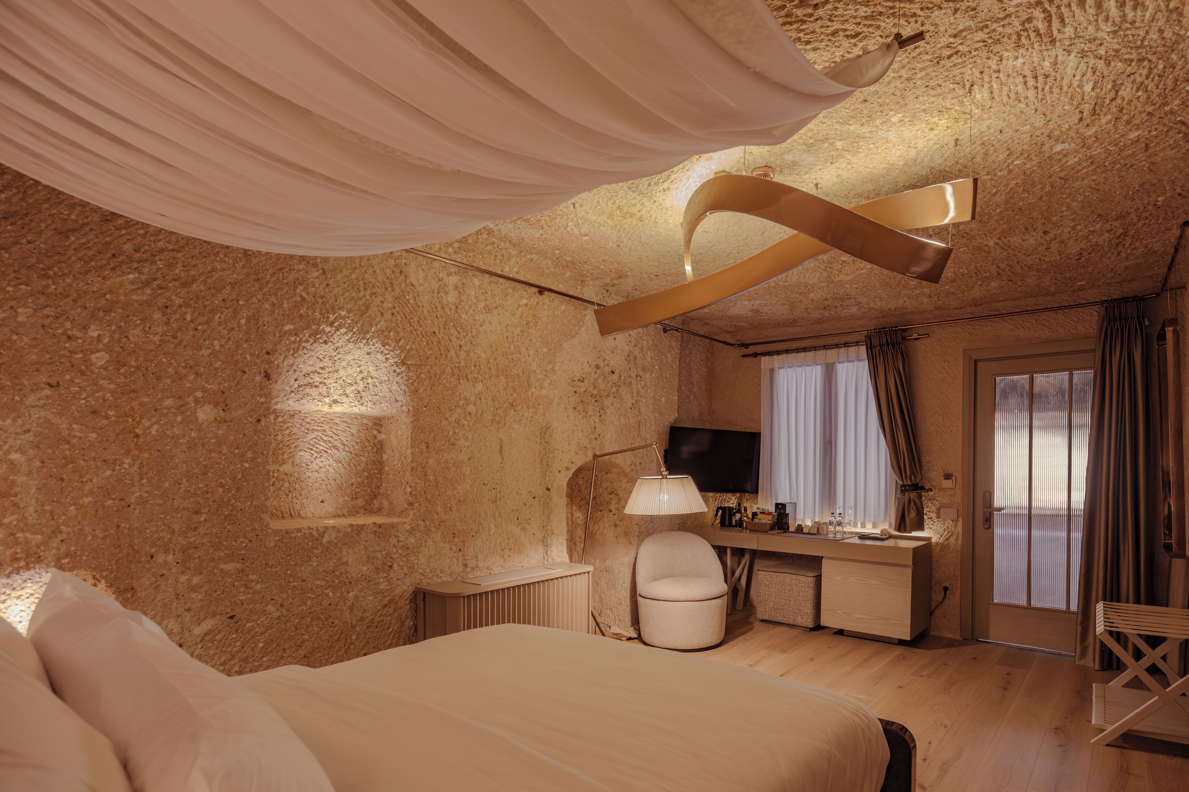 A bedroom with a bed, a desk, a chair, a TV, and a window with curtains.