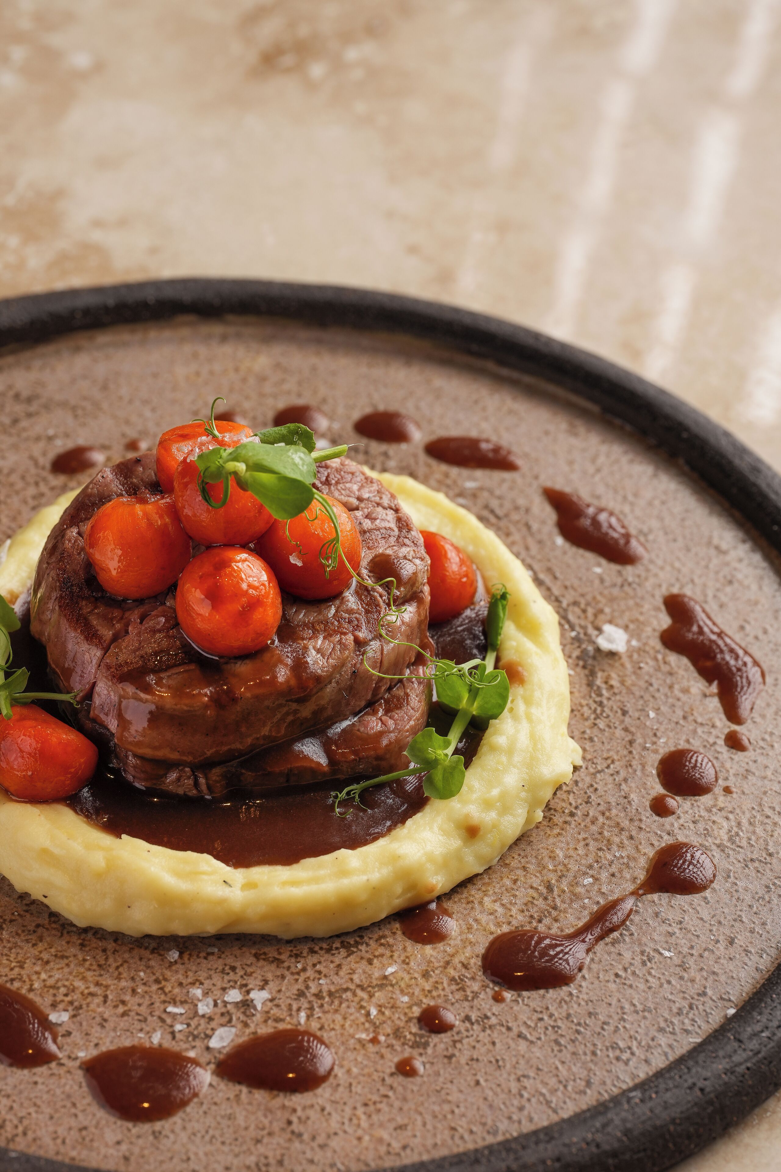 A steak with cherry tomatoes and a sauce on a plate with mashed potatoes.
