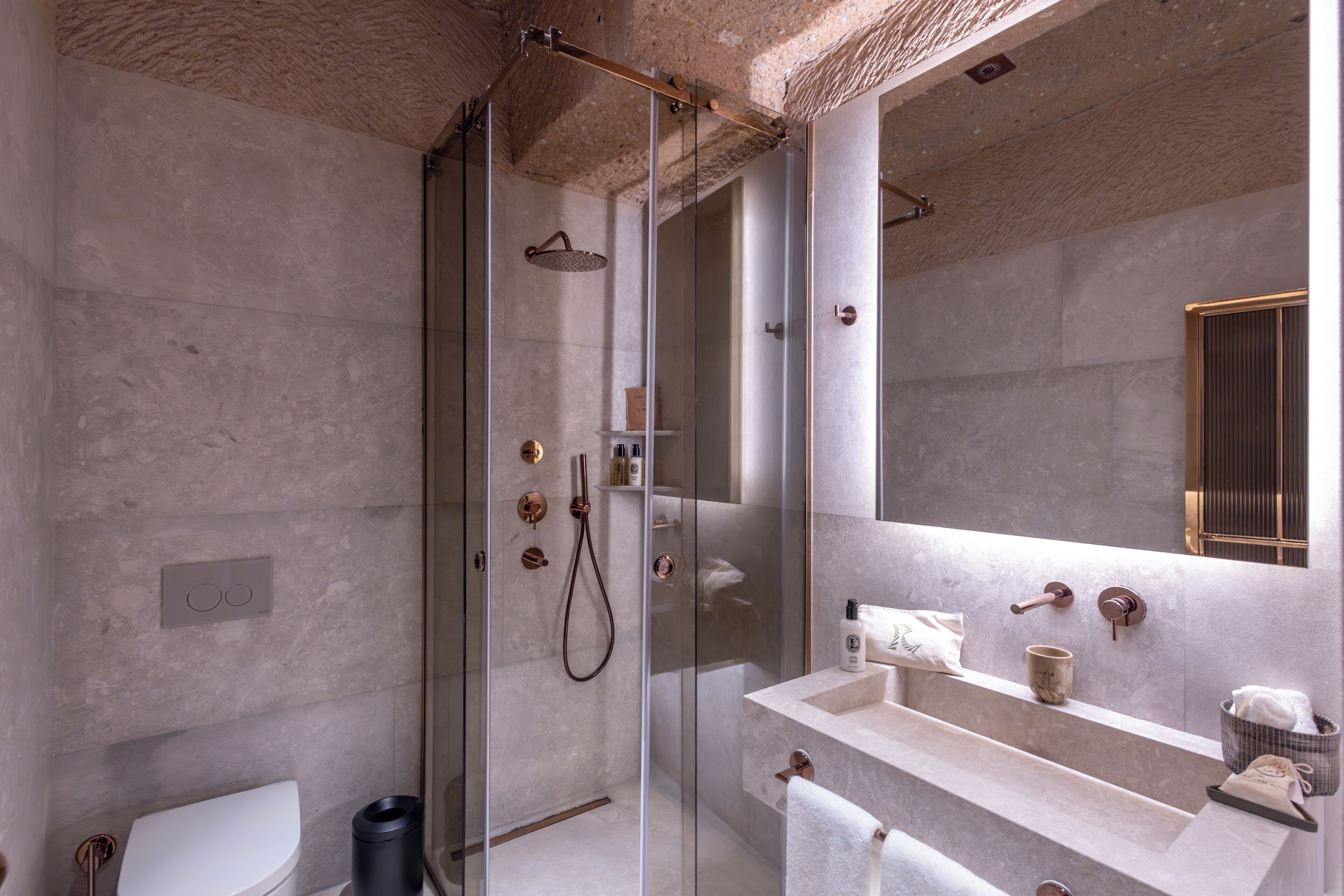 A modern bathroom with a glass-enclosed shower, a white toilet, and a marble sink with a towel rack.