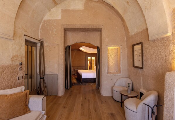 A cozy room with a bed, two chairs, a small table, and a door leading to another room. - Avantgarde Refined Caves of Cappadocia, Member of Small Luxury Hotel of the World (Ürgüp)