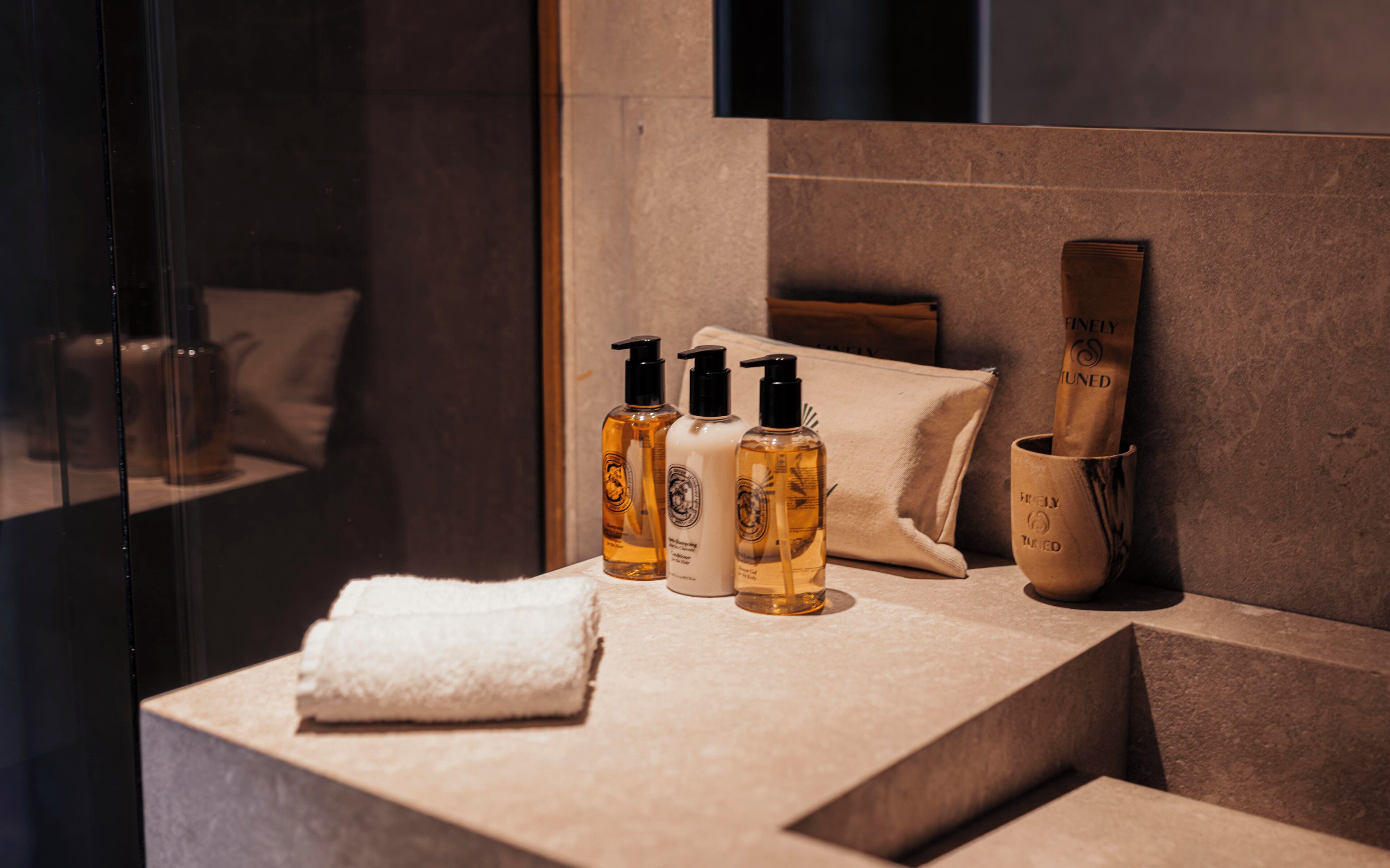 A bathroom with a marble counter, three bottles of liquid soap, a folded towel, and a wooden brush in a cup.