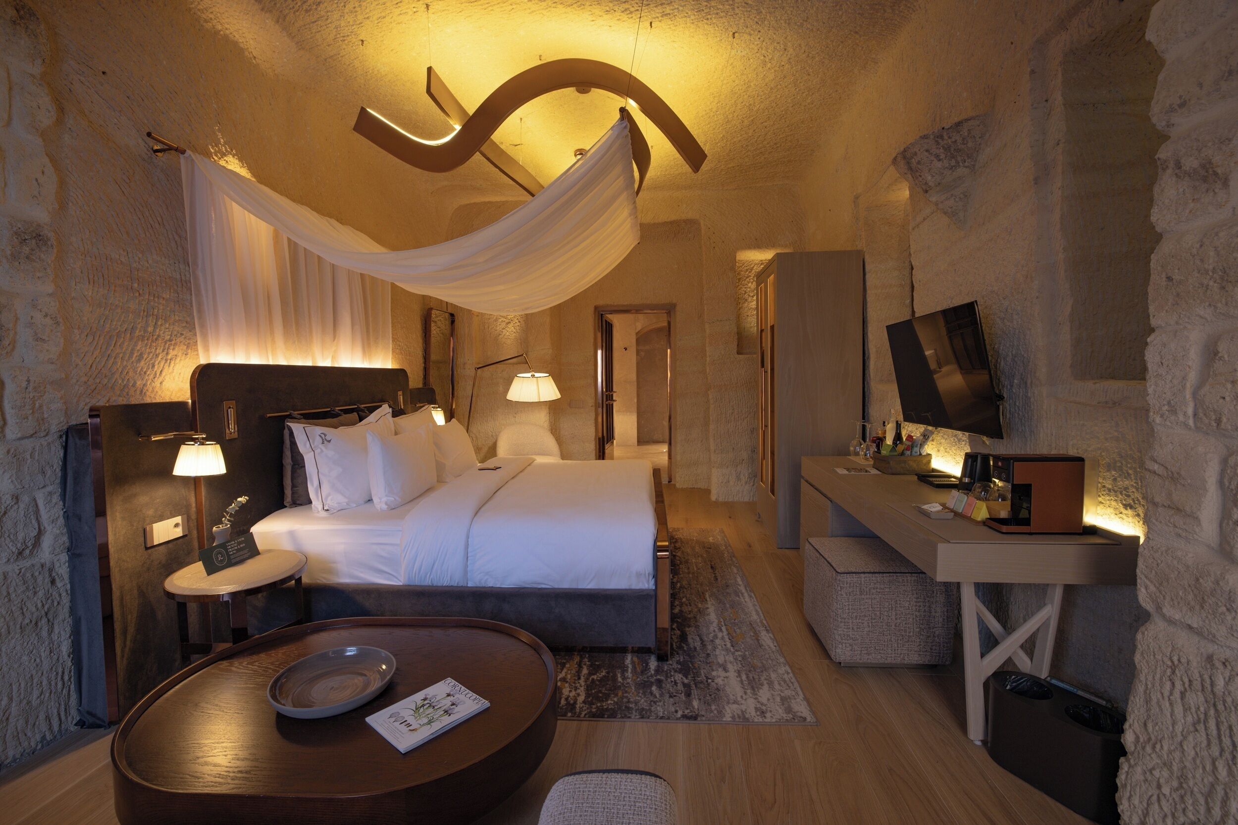 A modern hotel room with a bed, bedside tables, a desk, and a television.