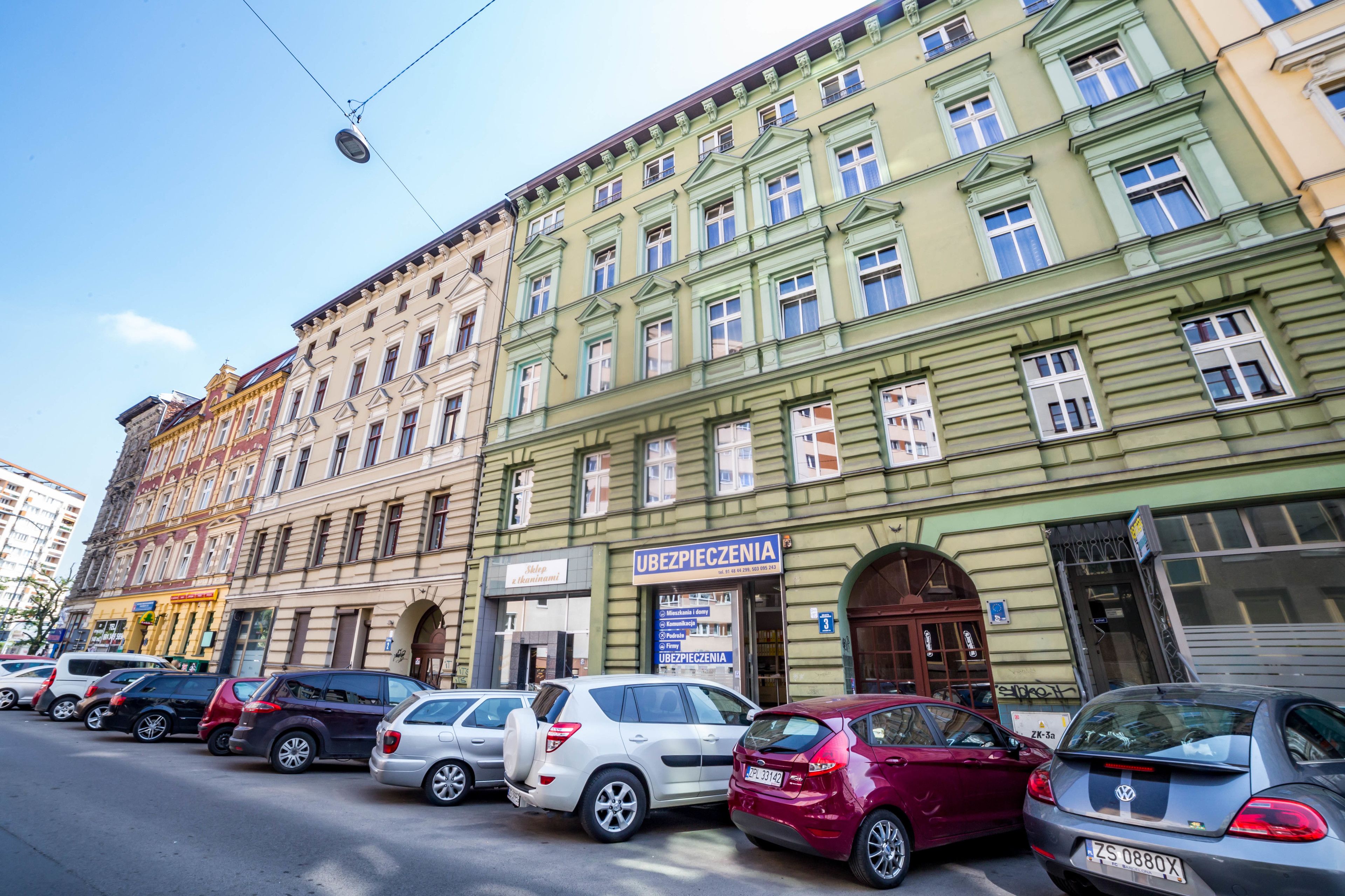 A row of parked cars in front of a building with a sign that reads "Ubezpieczenie".