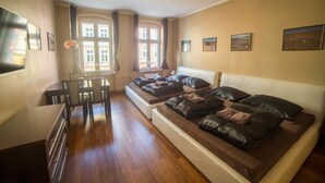 Un dormitorio con una cama grande, un escritorio y una silla. Hay ventanas con cortinas, una lámpara en el techo y cuadros en la pared.