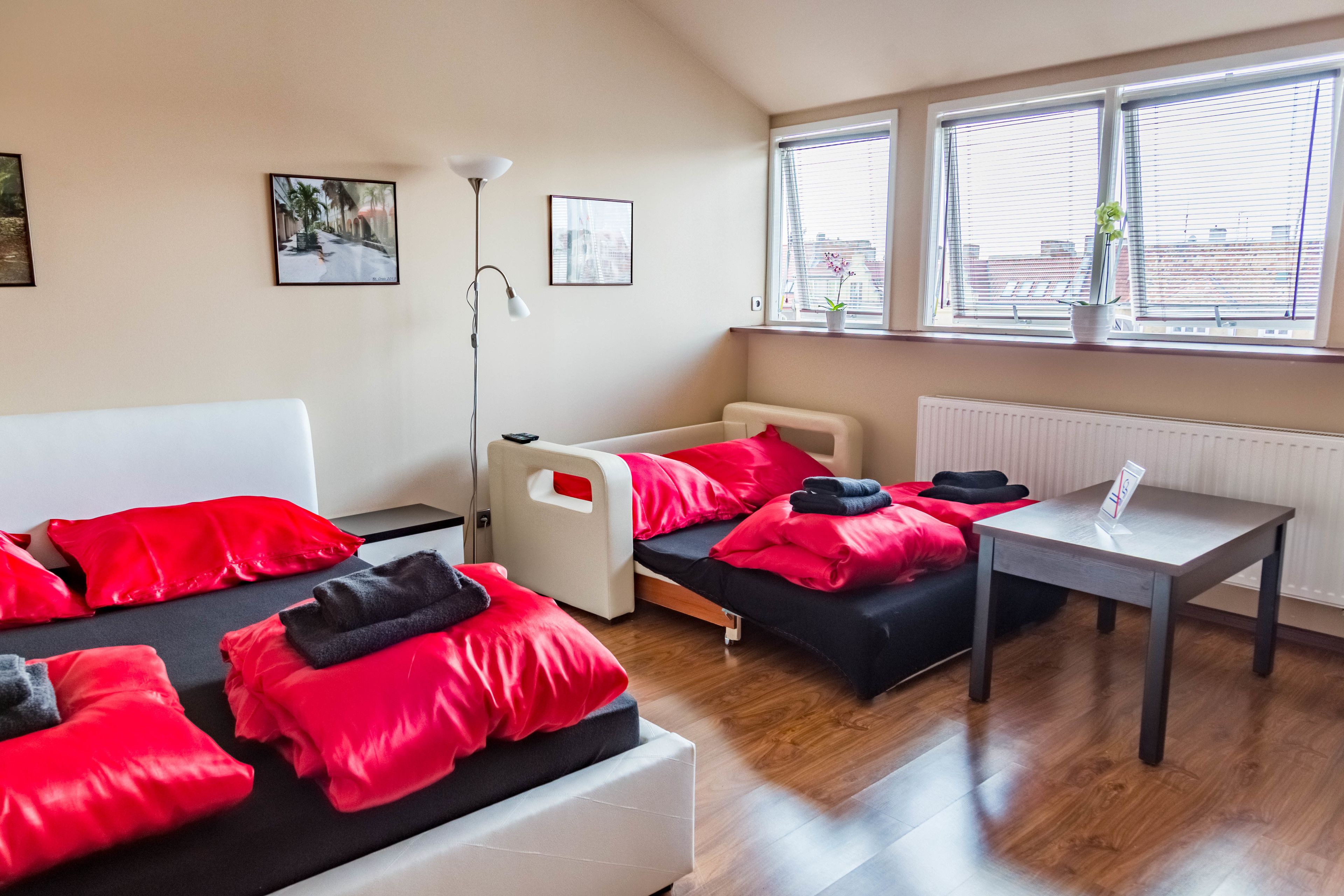 A hotel room with two beds, a bedside table, a floor lamp, and a window with blinds.
