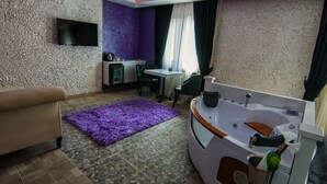 Ein modernes Badezimmer mit einer Badewanne, einem Waschbecken und einer Toilette. Ein Fernseher ist an der Wand befestigt und ein kleiner Tisch mit Stühlen steht bereit.