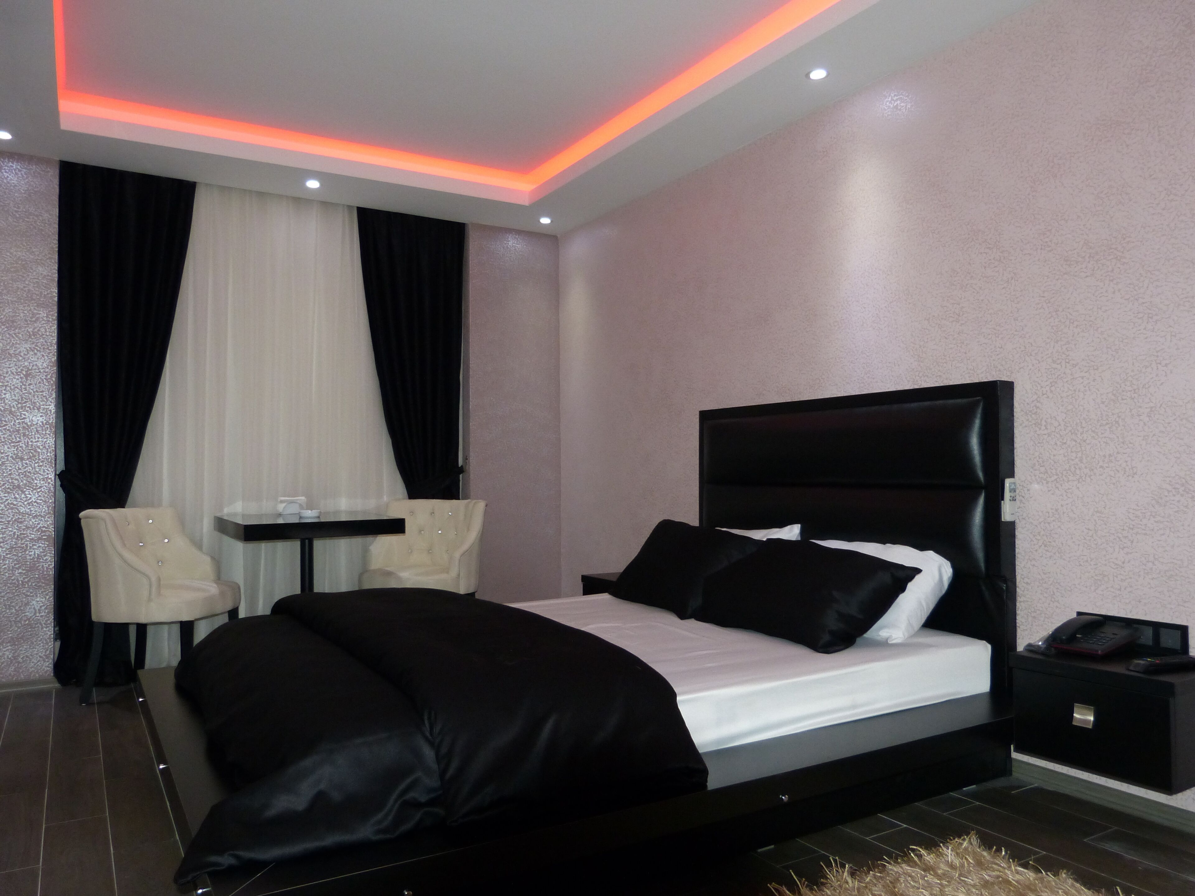 A modern bedroom with a black bed, a small table, two chairs, and a nightstand with a phone.