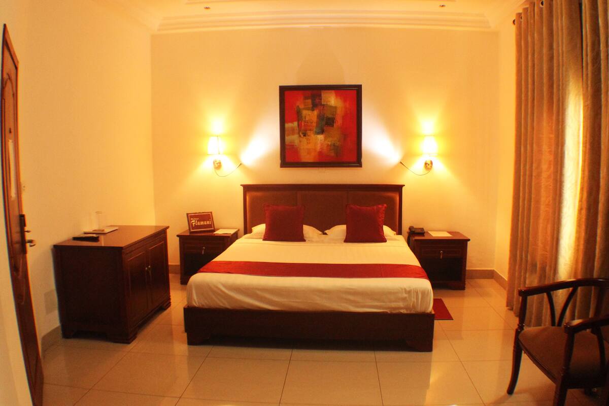 A hotel room with a large bed, two bedside tables, a nightstand, a chair, and a painting on the wall.