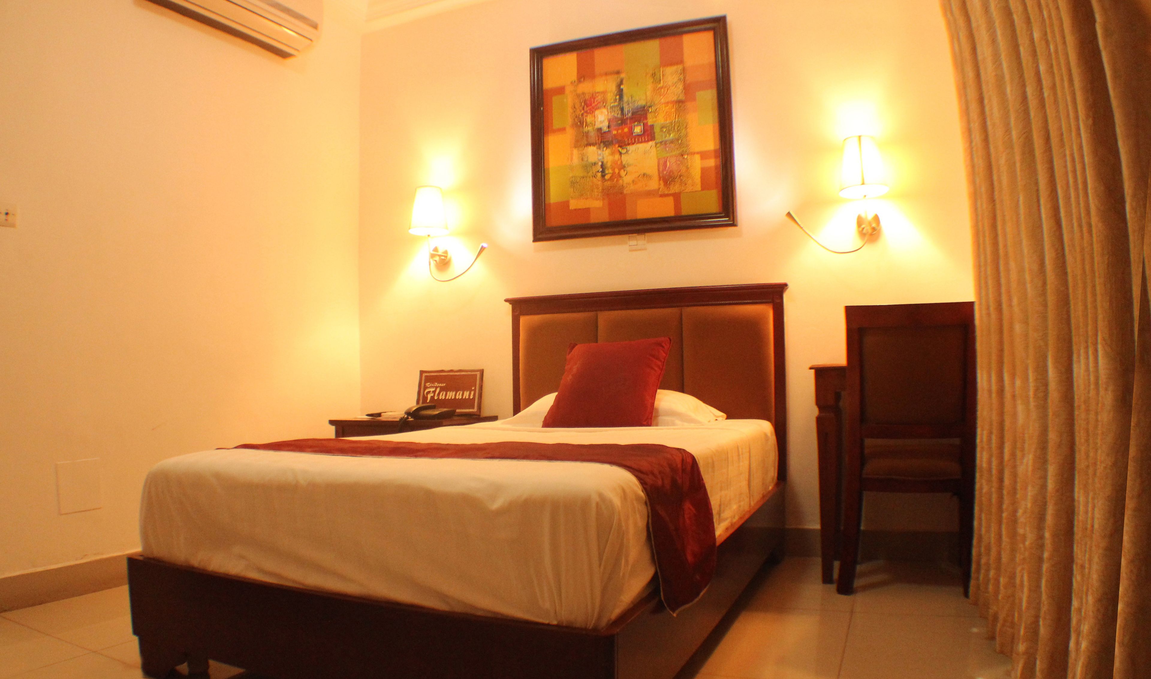 A hotel room with a bed, a nightstand, a lamp, a painting on the wall, and a curtain.