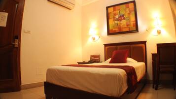 A hotel room with a bed, bedside lamps, a nightstand, a chair, and a painting on the wall.