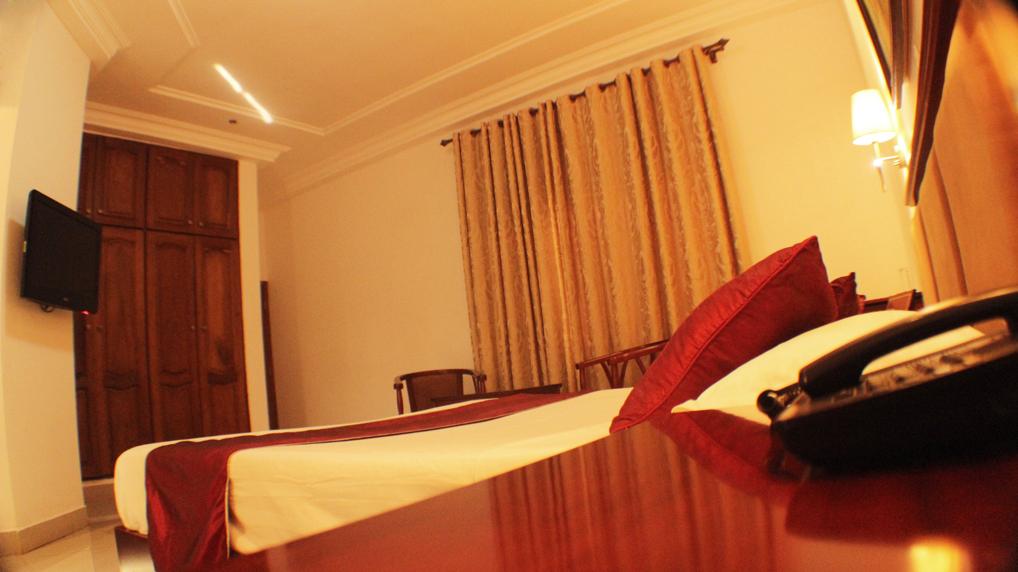 A hotel room with a bed, a desk with a telephone, a chair, a television on the wall, and a window with curtains.