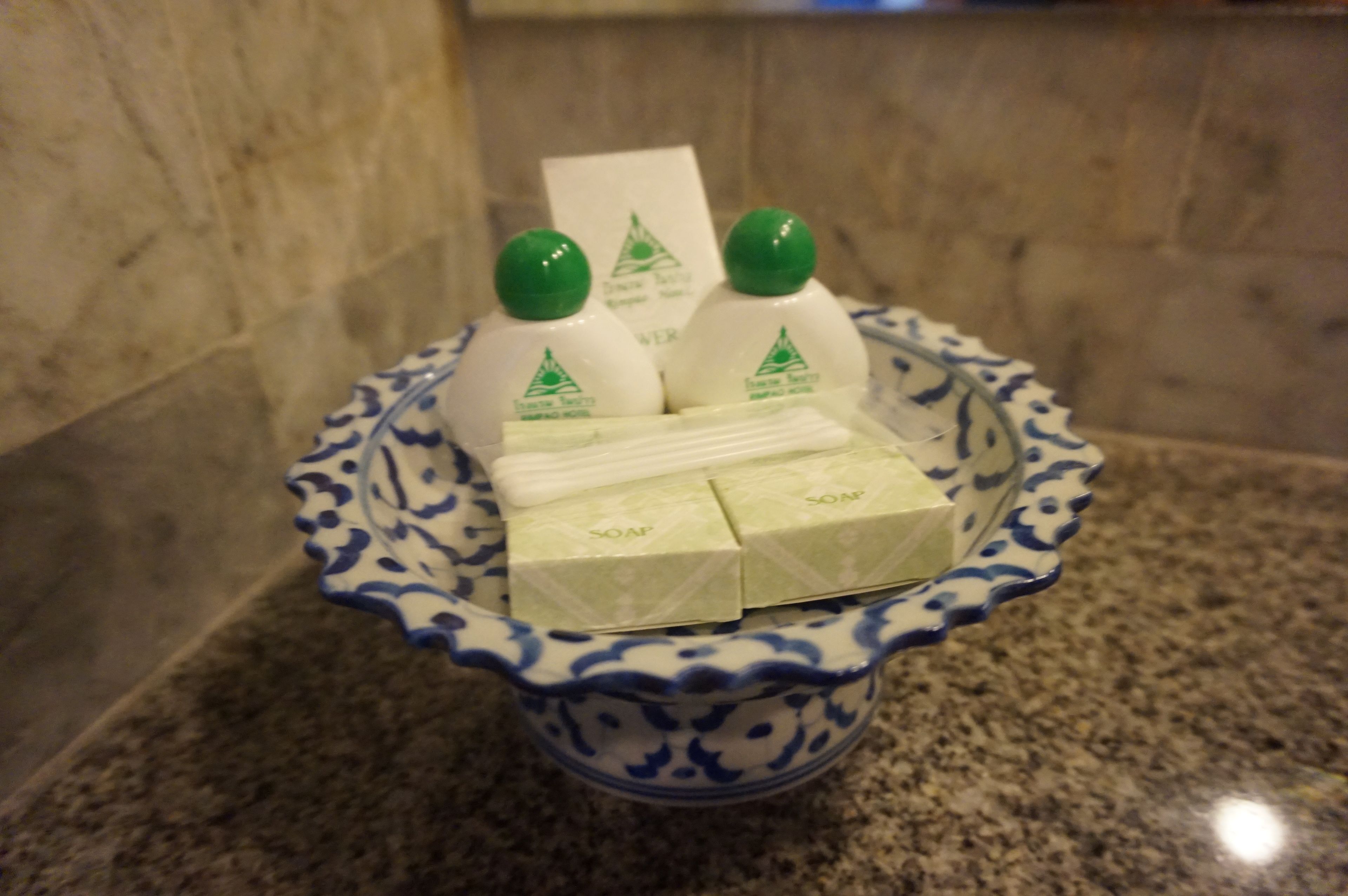 Un bol en céramique aux motifs bleus et blancs contenant trois bouteilles de savon et quelques pains de savon.