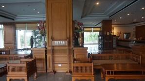 A spacious lobby with wooden furniture, a reception desk, and large windows allowing natural light.