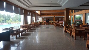 A spacious lobby with wooden furniture and large windows offering a view of greenery outside.