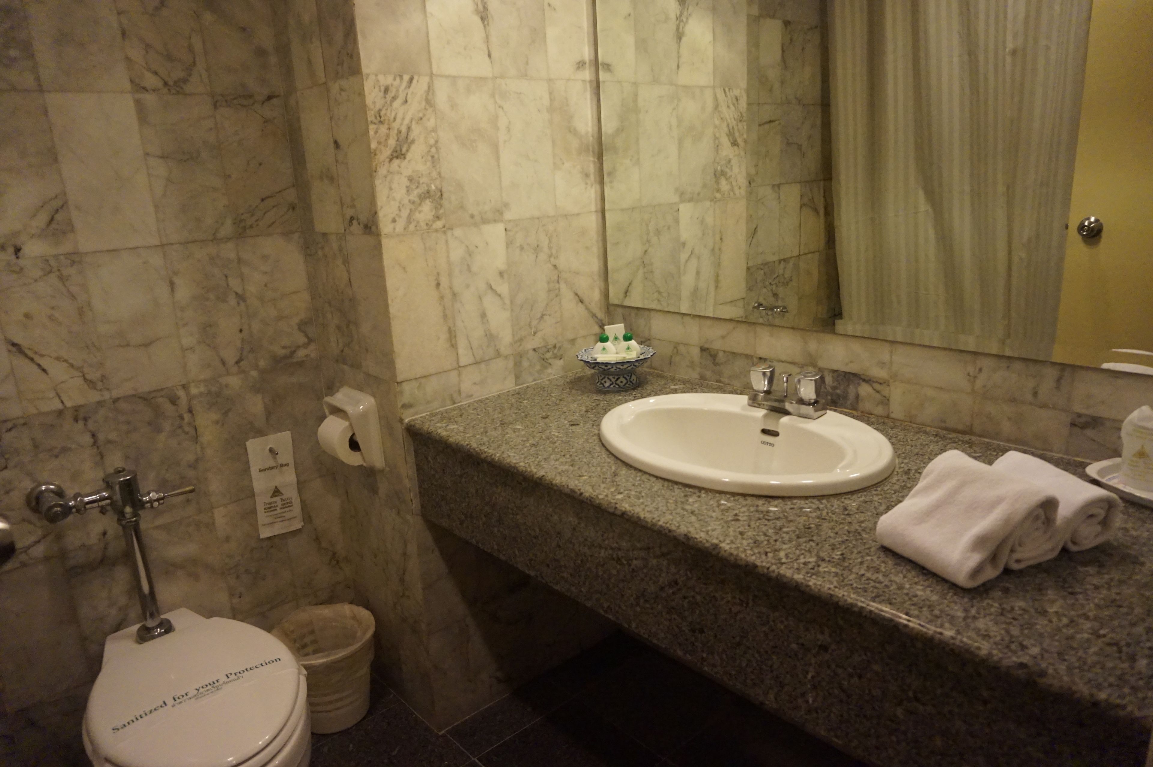 A bathroom with a marble floor, a white sink, a mirror, and a toilet.