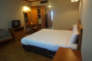 A bedroom with a bed, a television on a wooden stand, a chair, a desk, and a wardrobe.