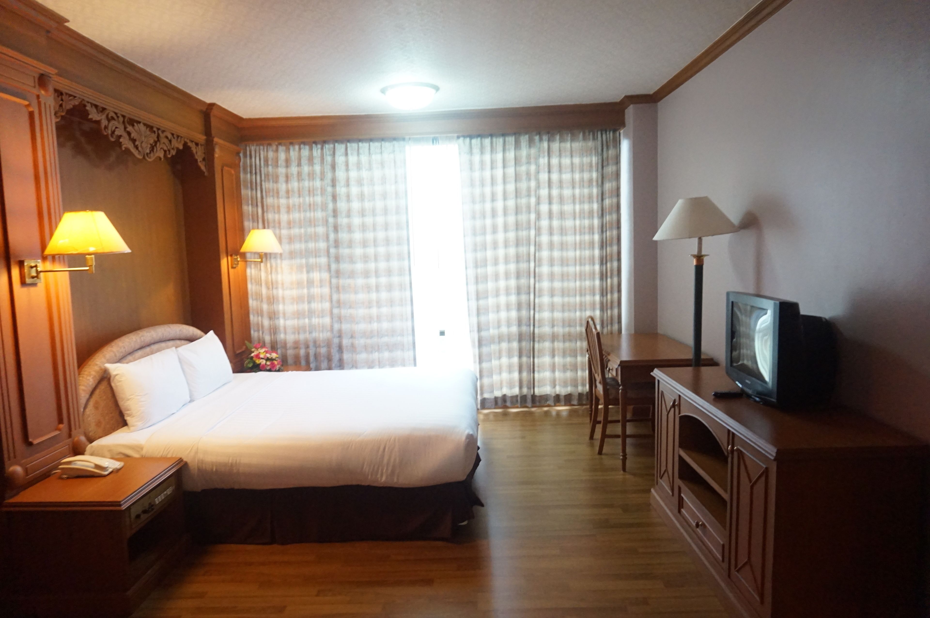 A hotel room with a large bed, bedside lamps, a television, a desk, and a chair.