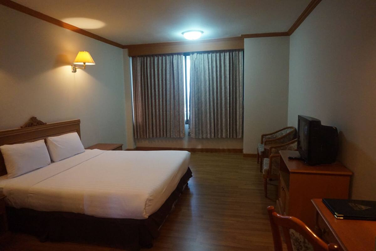 A hotel room with a large bed, a desk with a television, and a window with curtains.