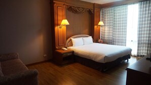 A hotel room with a large bed, wooden headboard, two bedside lamps, a nightstand with a phone, and a wooden desk.