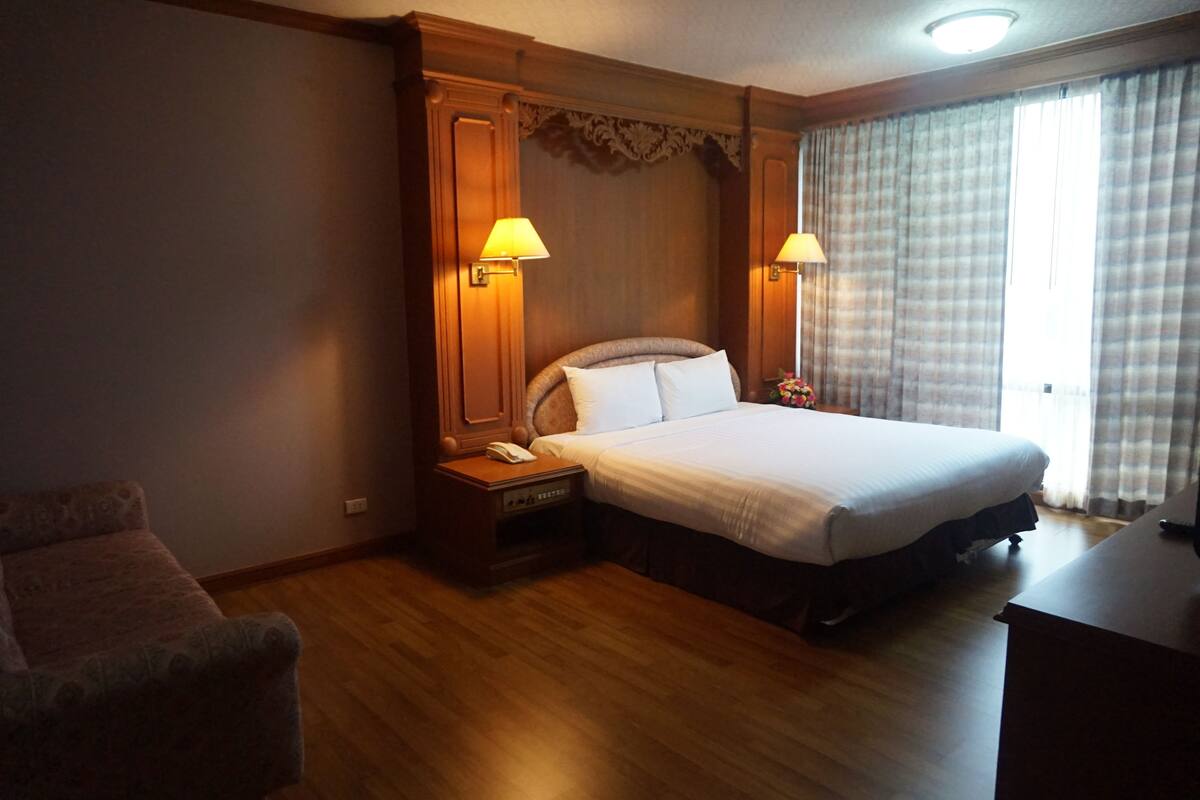 A hotel room with a large bed, wooden headboard, two bedside lamps, a nightstand with a phone, and a wooden desk.