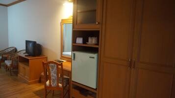 Una habitación con armarios de madera, un refrigerador pequeño, un televisor sobre un mueble de madera y una silla con estampado floral.