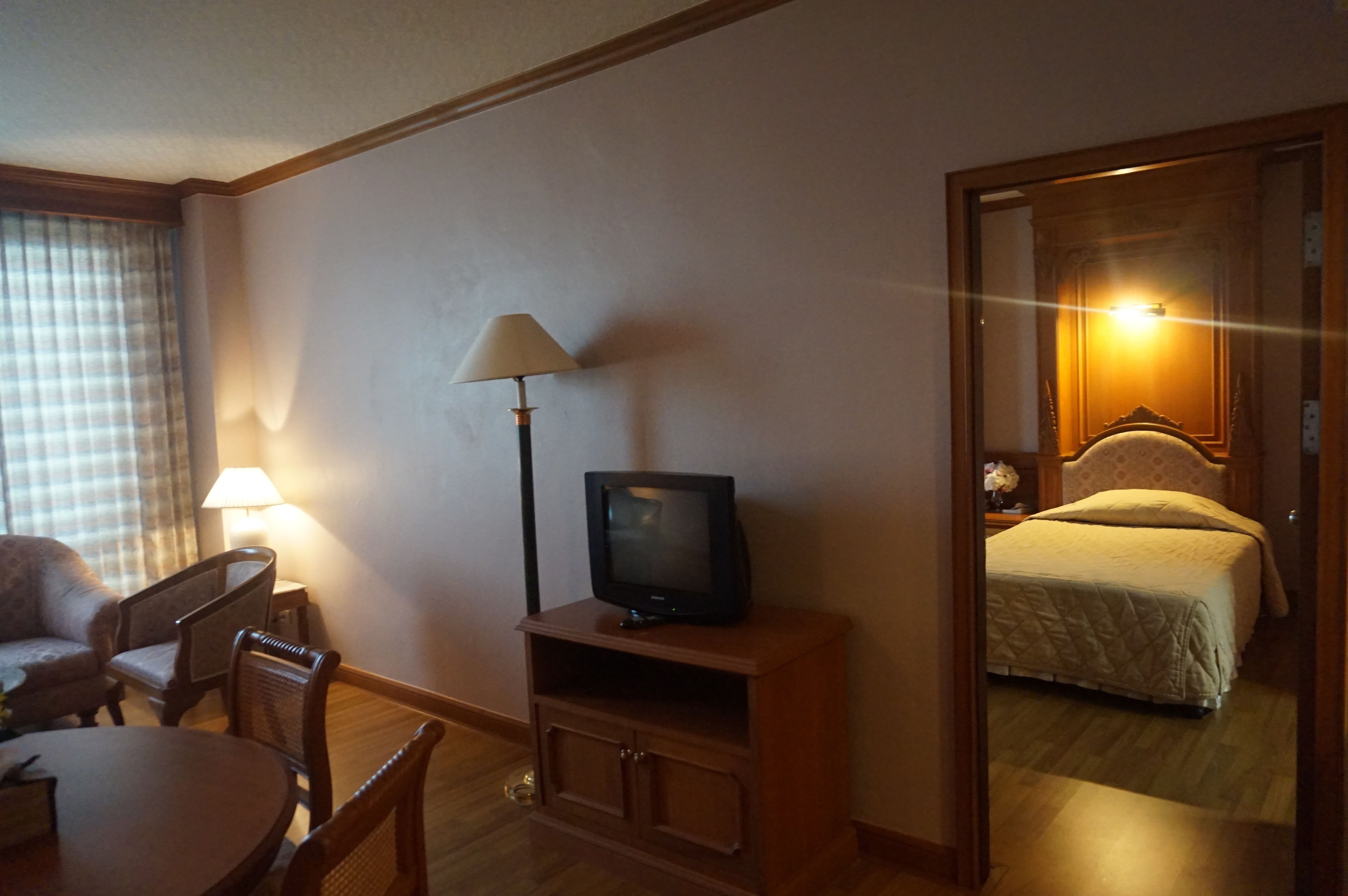Ett hotellrum med en tv på ett träställ, en lampa, en säng och en matplats med stolar och ett bord.