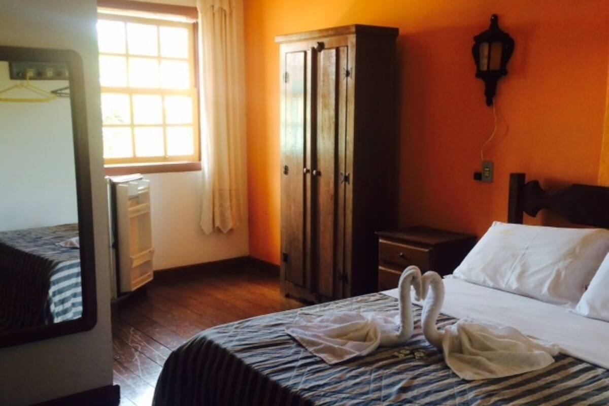 Una habitación de hotel con cama, armario, mesita de noche y ventana con cortinas.