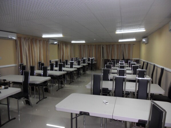 A conference room with multiple tables and chairs, arranged in rows.