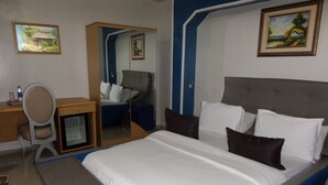 A hotel room with a bed, a desk, a chair, and a wardrobe. - Primal Hotel Ikeja GRA (Lagos)