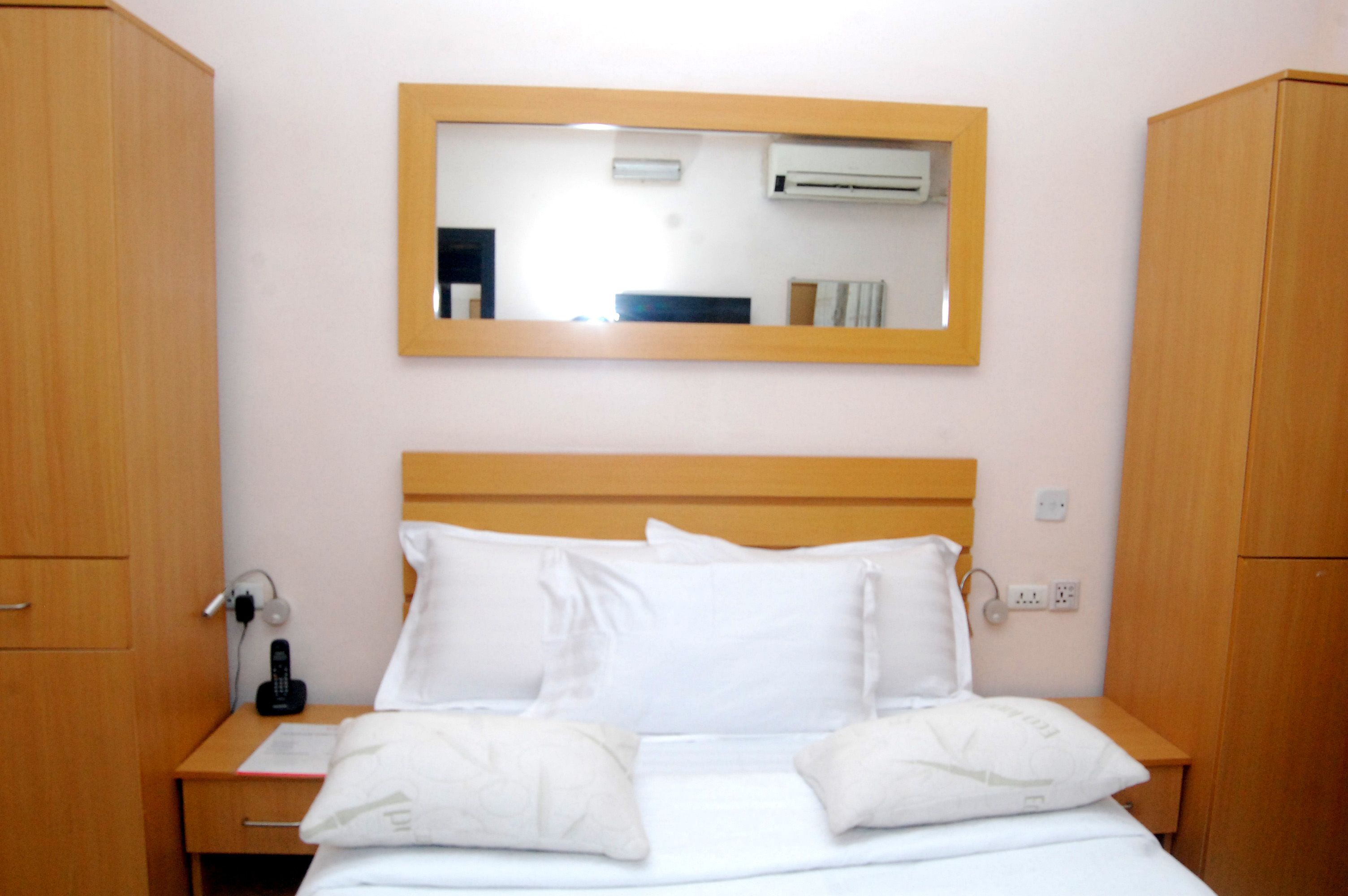 A hotel room with a wooden headboard, a bedside table with a phone, and a mirror on the wall.