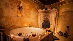 A stone-floored bathroom with a freestanding bathtub, candles, and a bowl of fruit. - Sunak Cave Hotel (Ürgüp)