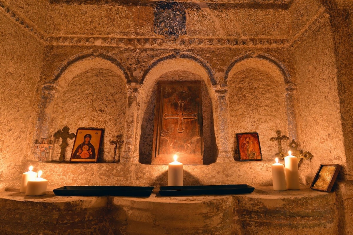 A dimly lit chapel with three arched niches, each containing religious icons and candles.