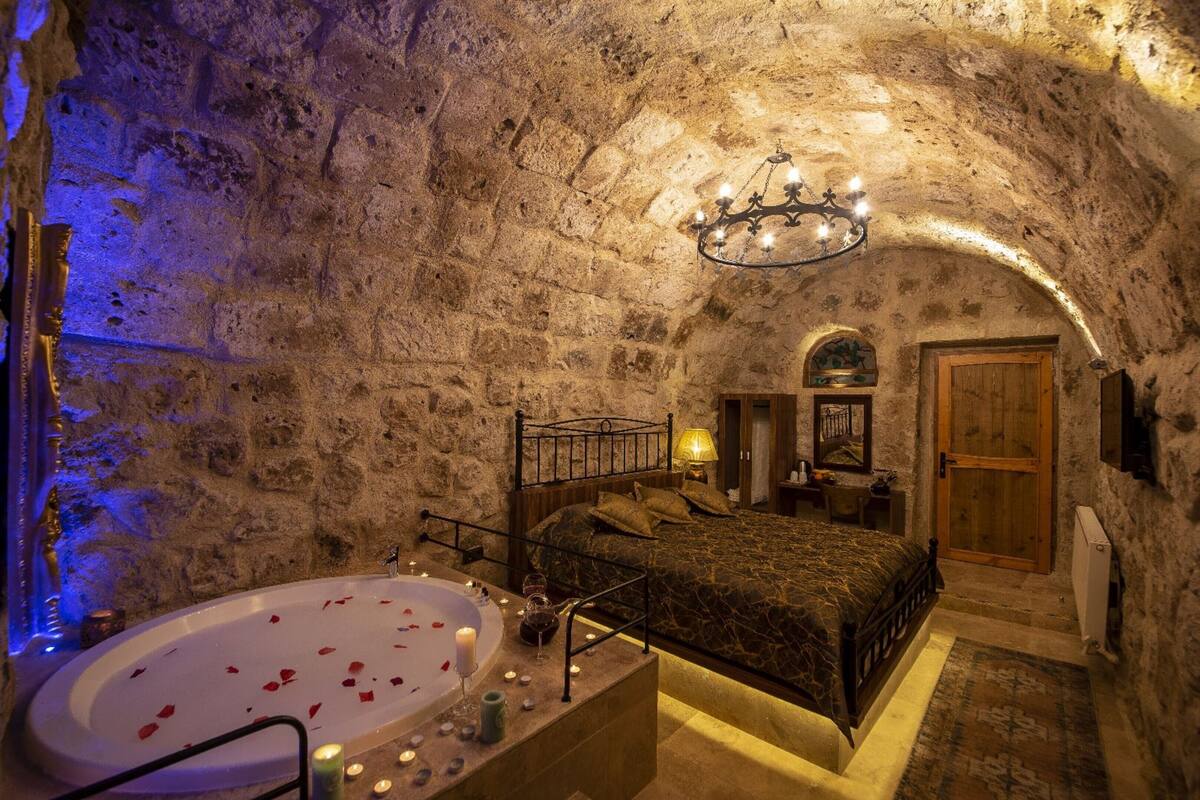 A stone-walled bedroom with a large bed, a wooden door, and a chandelier.