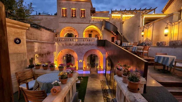 An outdoor dining area with stone benches and tables, surrounded by potted plants and a stone wall. - Sunak Cave Hotel (Ürgüp)