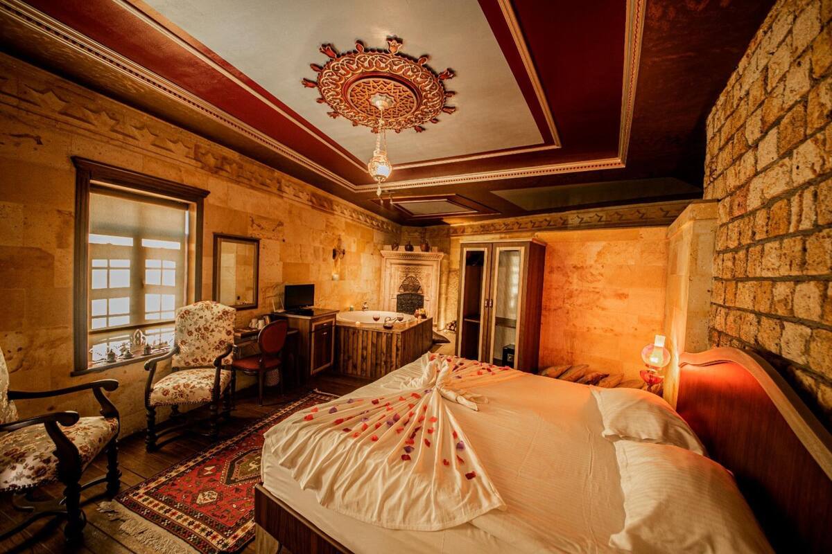 A room with a large bed, a desk with a chair, a bathtub, and a fireplace.