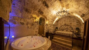 A spa room with a stone wall, a bathtub, candles, and a chandelier. - Sunak Cave Hotel (Ürgüp)