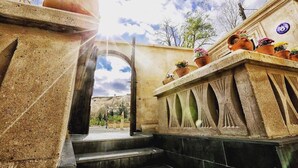A stone archway leading to a courtyard with terracotta pots and a view of a mountainous landscape. - Sunak Cave Hotel (Ürgüp)