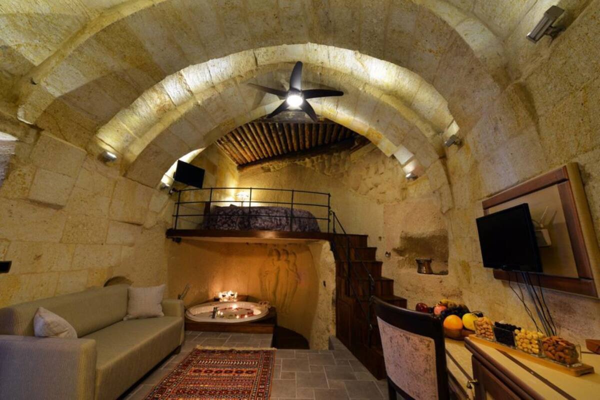 A cozy room with a stone ceiling, a wooden bench, a small table with fruit, and a television on the wall.