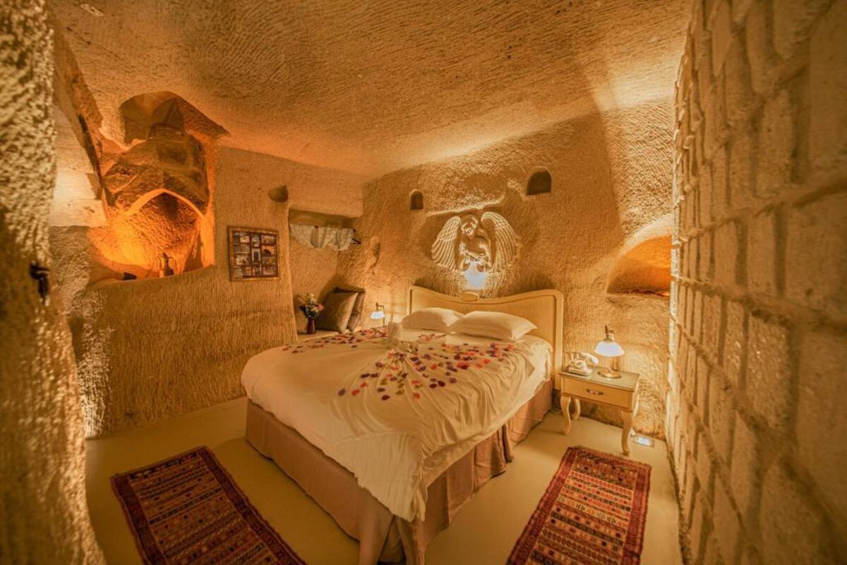 A stone-walled room with a bed, a nightstand, and a wall-mounted lamp.
