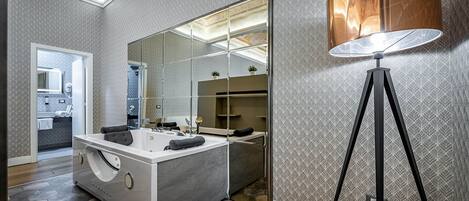 A modern bathroom with a large mirror, a freestanding bathtub, and a floor lamp.