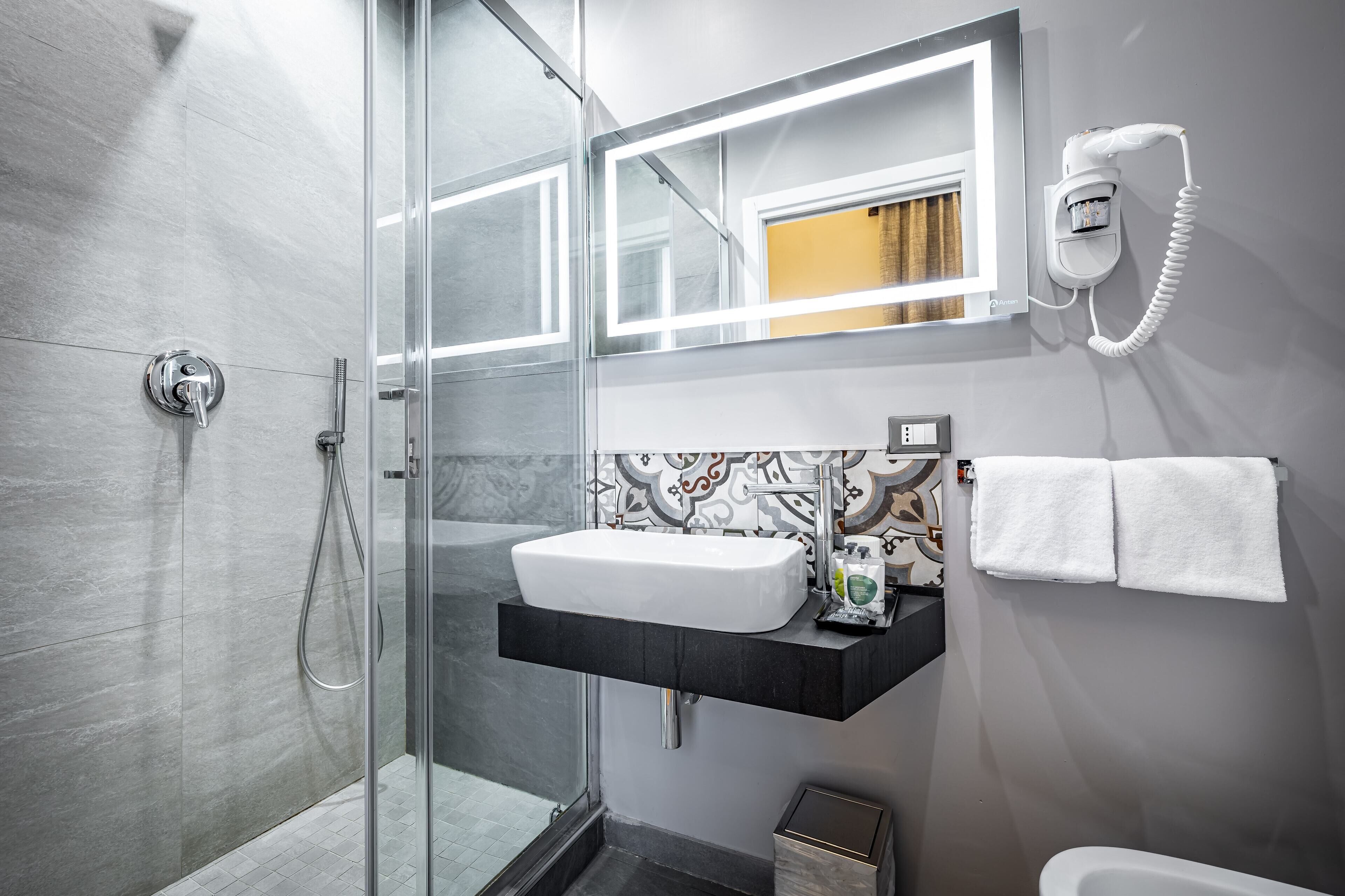 Un baño moderno con cabina de ducha de vidrio, un lavamanos blanco y un perchero para toallas.