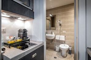 A modern kitchen with a built-in stove and a coffee maker, and a bathroom with a sink, bidet, and towel rack. - Martelli 6 Suites and Apartments (Florence)