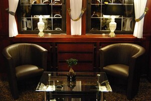 Una habitación con dos sillones de cuero, una mesa de vidrio con un florero y un ventanal con dos lámparas.