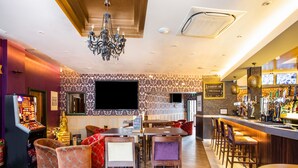 Una zona de bar con taburetes, una barra y un televisor montado en la pared.