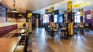 Un restaurante con suelo de madera, zona de bar y diferentes disposiciones de mesas.