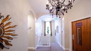 Un pasillo de hotel con un candelabro, un adorno en la pared con forma de sol, una escalera y una puerta con la leyenda 'ROOM 101-103'.