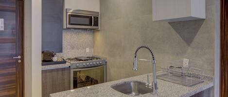 A compact kitchen with a granite countertop, stainless steel sink, microwave, stove, and oven.