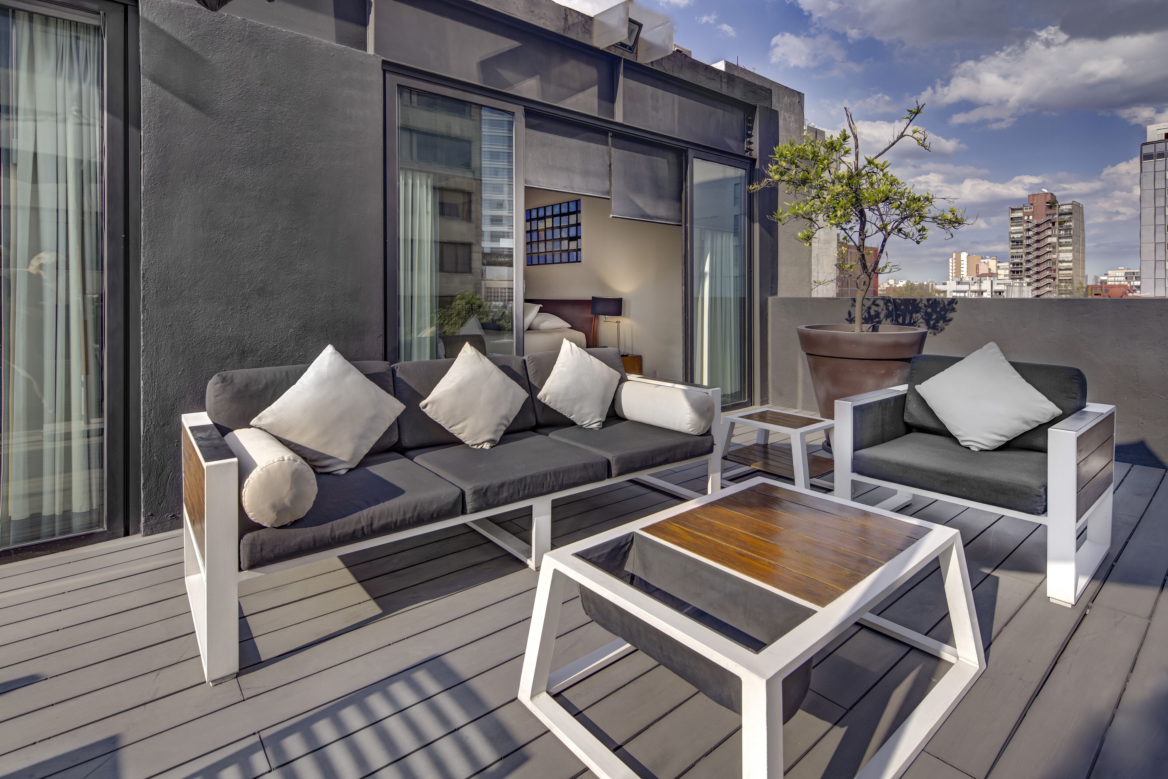 Un área de estar moderna al aire libre con un sofá y una mesa de centro, una planta en maceta y vistas de la ciudad.