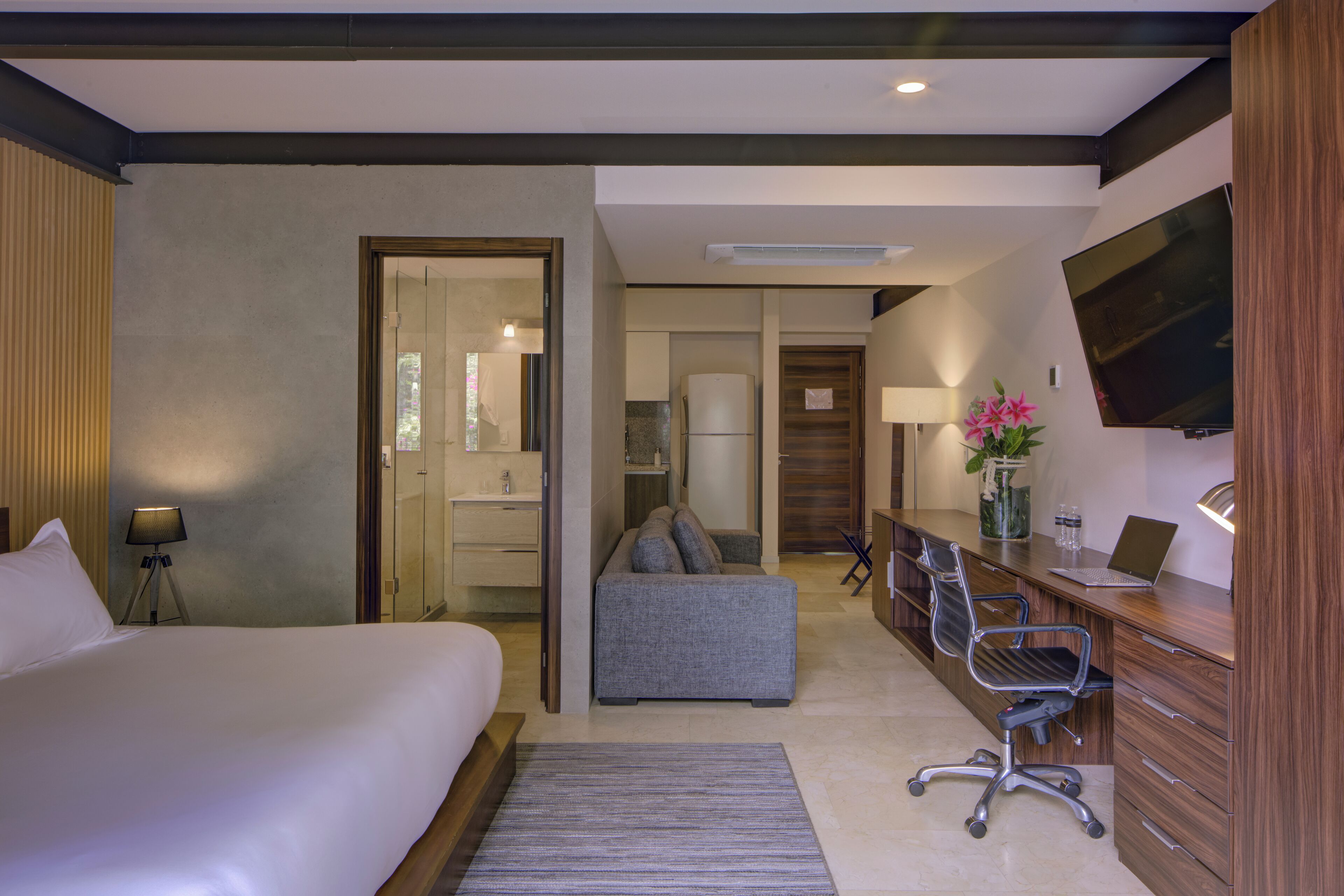 Une chambre d’hôtel moderne équipée d’un grand lit, d’un canapé, d’un bureau avec un ordinateur portable et d’une télévision.